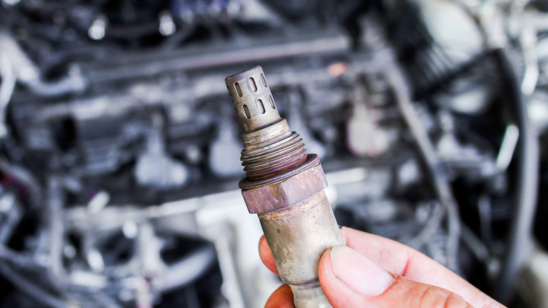 A hand holding an oxygen sensor for a car