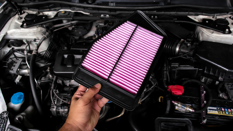 A person holding a brand new engine air filter that is about to be installed