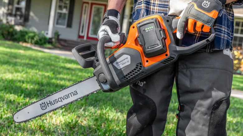 close-up of a worker holding a Husqvarna 350i Power Axe chainsaw in the home's front yeard
