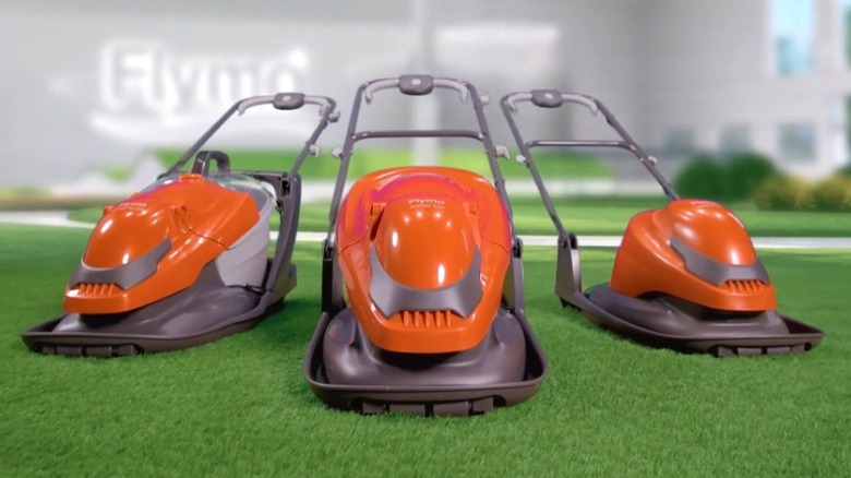 Three Flymo hover lawnmowers on grass.