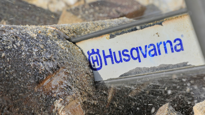 Close-up of Husqvarna chainsaw cutting through a log showing the company logo.