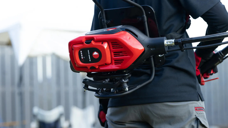 Close-up of Zenoah brush cutter hanging off a person's back.