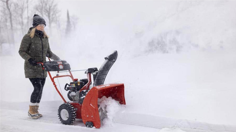 A person pushing a Troy-Bilt Storm 2420 snow blower in the snow.