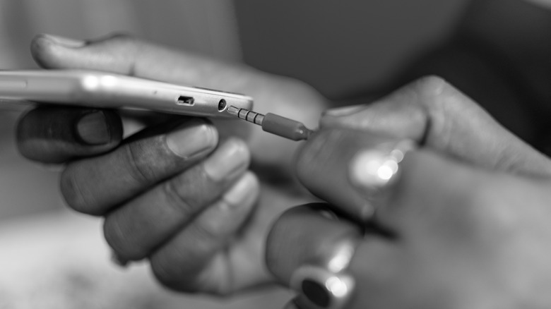 Person plugging wired earphones into a phone.