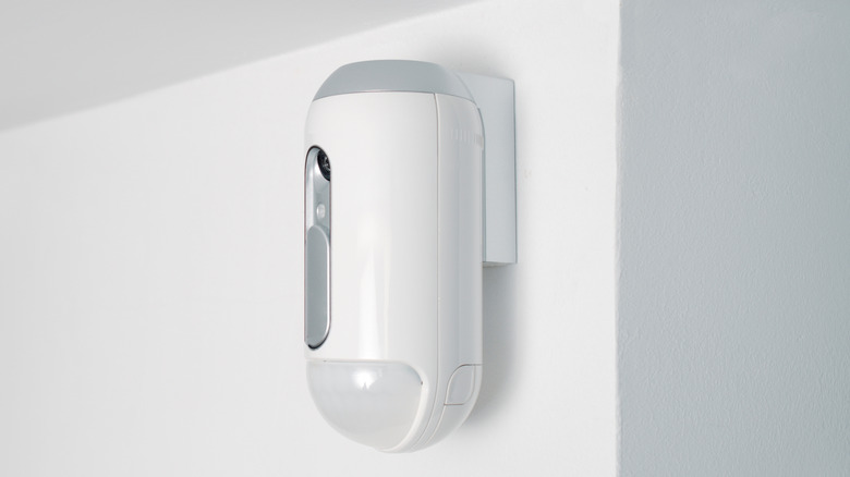 a motion detector equipped with a camera, mounted on a wall, indoors, as part of a burglar alarm system