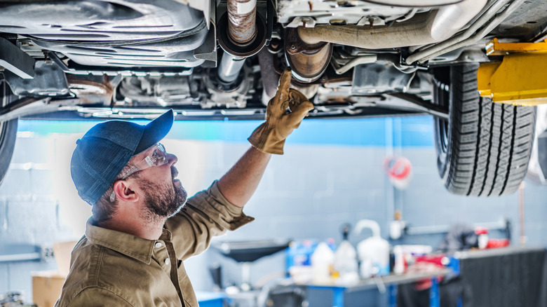 Mechanic pointing at catalytic converter on bottom of car that's up on a lift