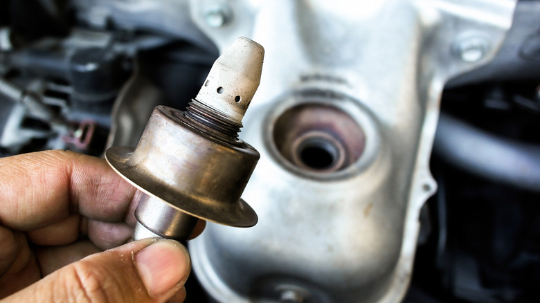 Hand holding oxygen sensor with catalytic convertor in background