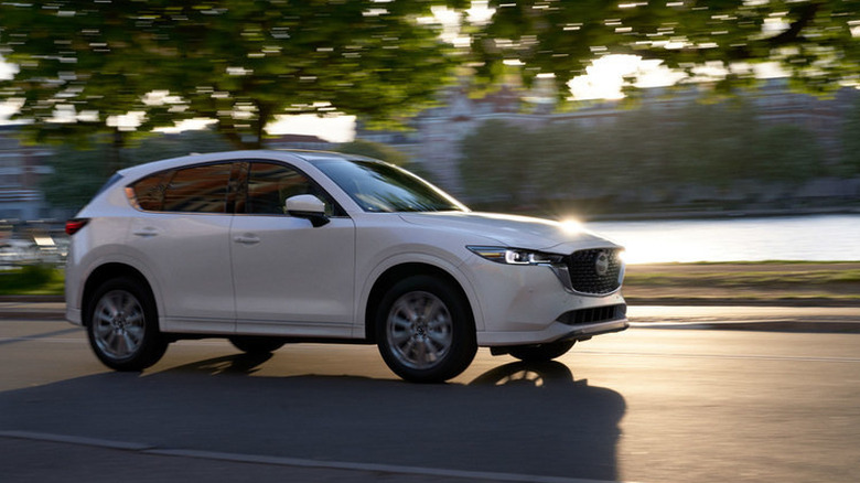 Slightly blurry white 2022 Mazda CX-5 moving on a road with water and foliage in the background