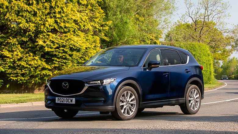 Blue 2021 Mazda CX-5 on a roadway with trees in the background