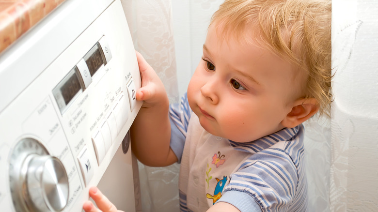 A young child pressing buttons on a white washing machine