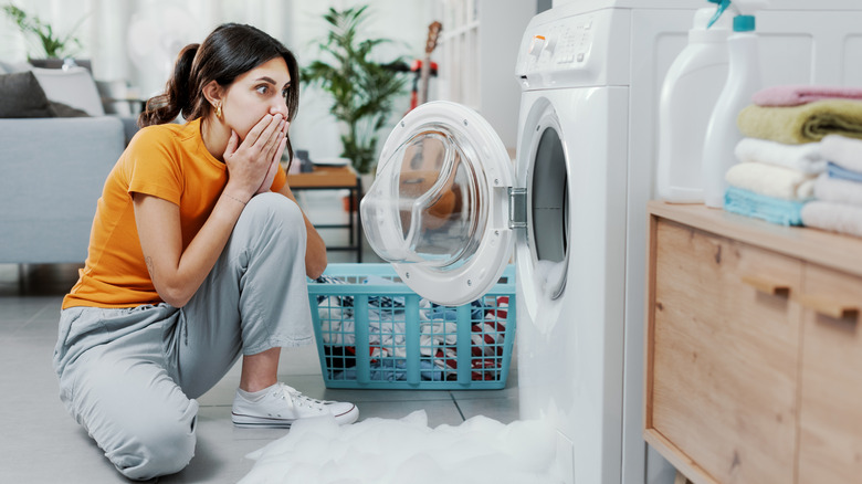 A woman sitting on the floor near a white washing machine that has overflowed