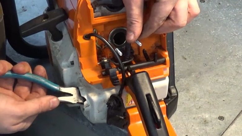A person replacing a Stihl chainsaw's fuel line.