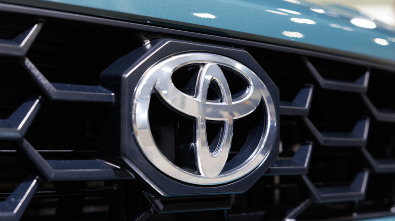 Close-up of a silver Toyota logo on a black grille on a light blue vehicle