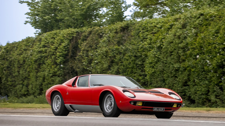 1968 Lamborghini Miura driving on country road with hedgerow in background, front-right 3/4 view