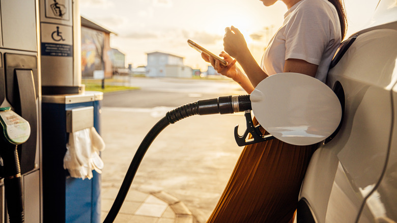 Person texting on phone leaning on car with gas station fuel nozzle inserted