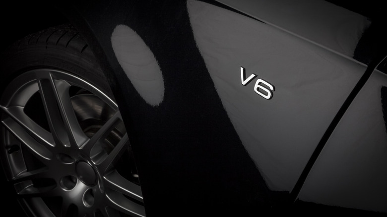 A close-up on a car's front fender showing a chromed "V6" badge.