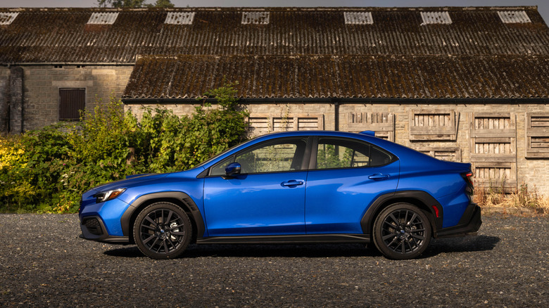 A side view of a blue 2026 Subaru WRX parked in front of an old barn