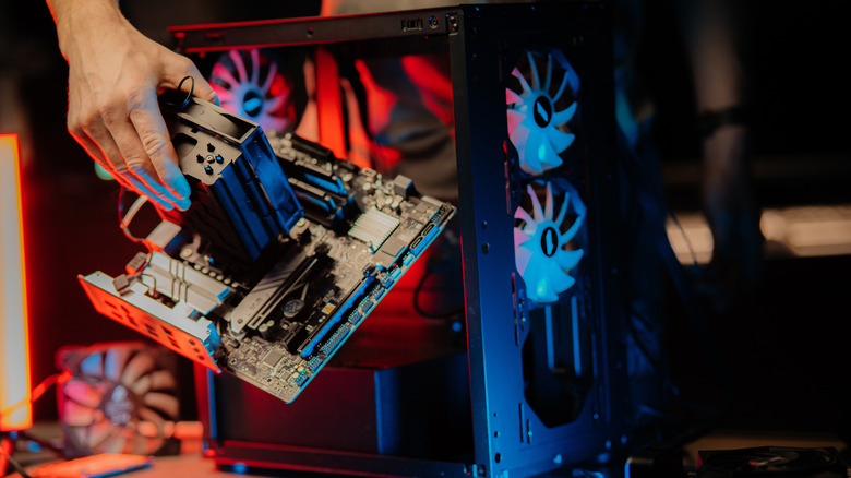 A hand holding a completed motherboard next to a PC desktop tower