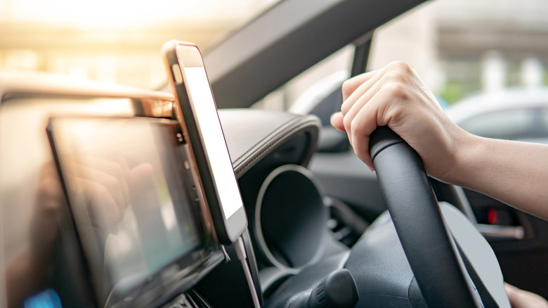 A phone attached near car's infotainment screen with a person's hand on steering wheel