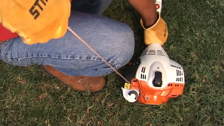 A man starting a STIHL trimmer by pulling the starter rope slowly on an Easy2Start model