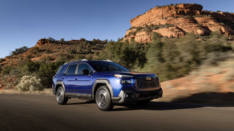 A 2026 blue Subaru Outback on the road with dramatic scenery behind it