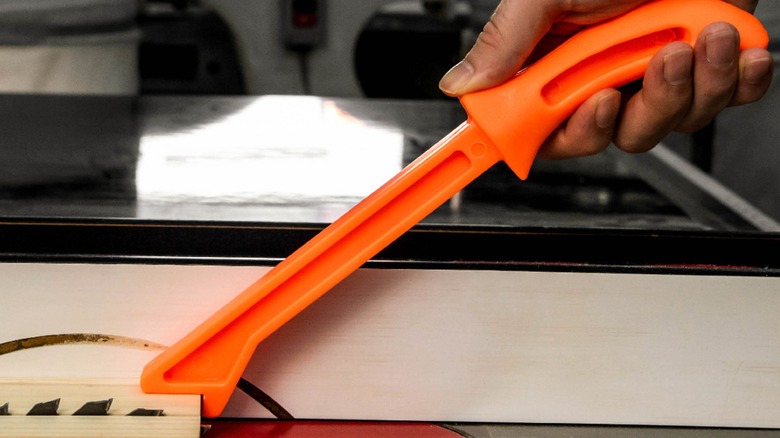 A person using an orange push stick on a table saw.