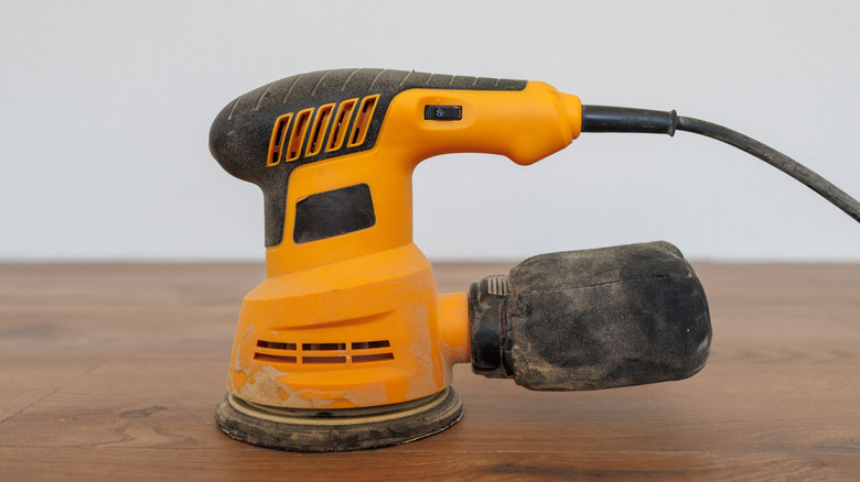 An orbit sander on a wooden surface.