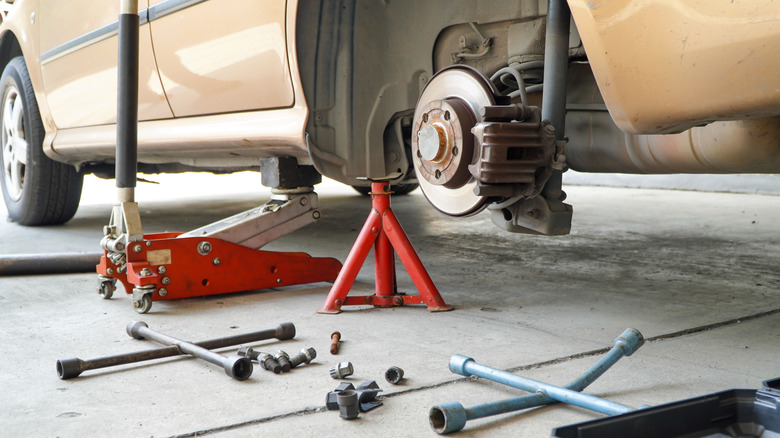 A floor jack and jack stand holding a up a car with a removed wheel