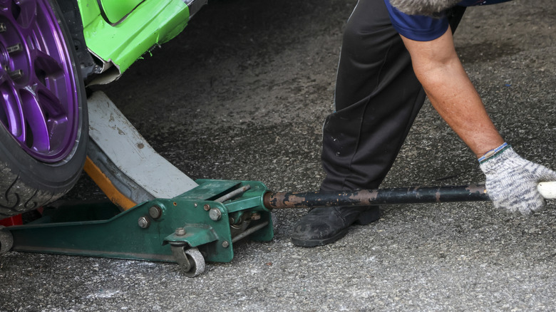 Person using a floor jack to lift a green car with purple rims