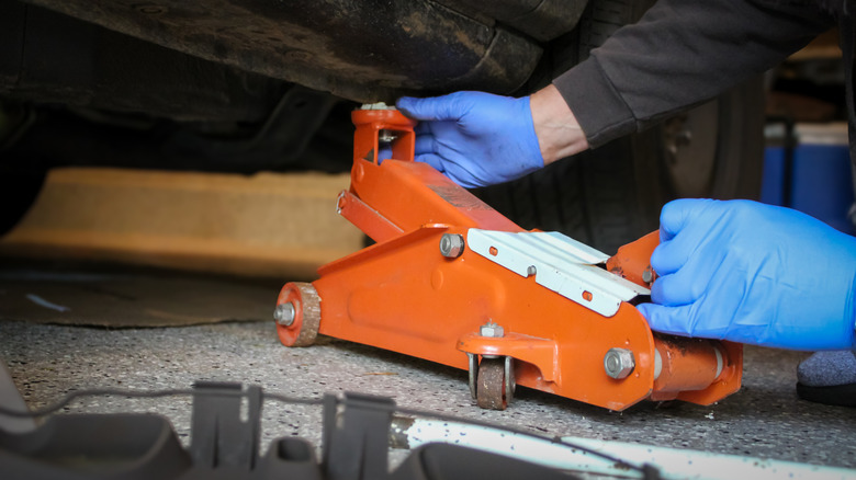 Person putting a floor jack into place to lift a vehicle