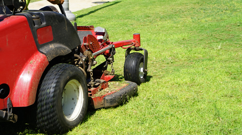 A person using a zero-turn mower to cut grass
