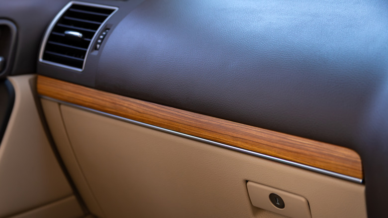 Close-up of a car's black and tan dashboard and glove compartment with a line of wood trim above it