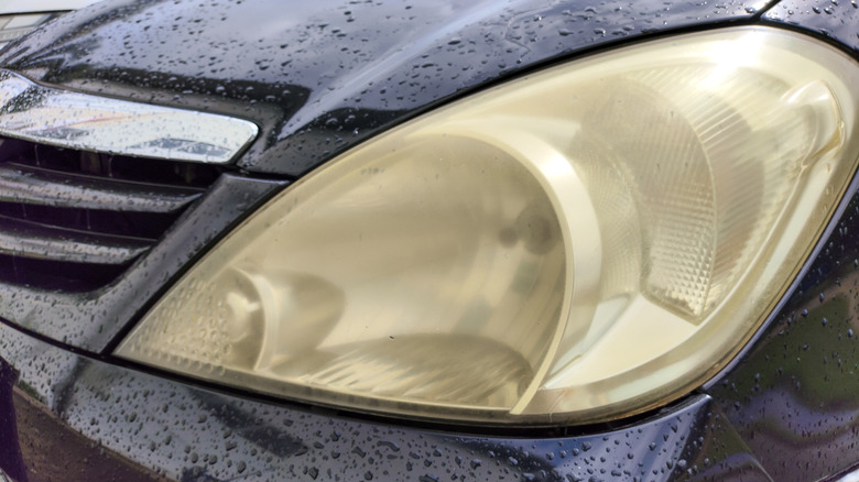 Close-up of a dirty, yellowed headlight on a wet, black vehicle