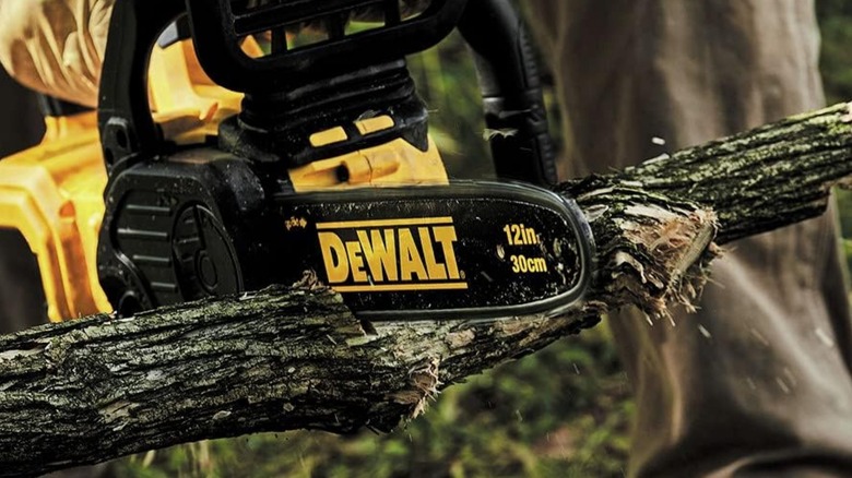 A closeup image of a person using a DeWalt 20-volt chainsaw to cut a tree limb