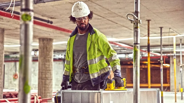 A worker carrying heavy materials using a DEWALT Grabo Suction Lifter.