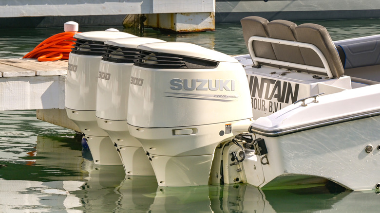 Three white Suzuki 300 outboard motors mounted on a boat docked beside a marina