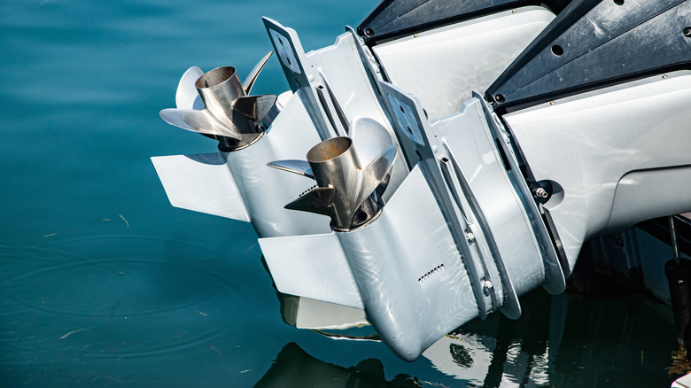 Two outboard boat motors with steel propellers tilted above seawater