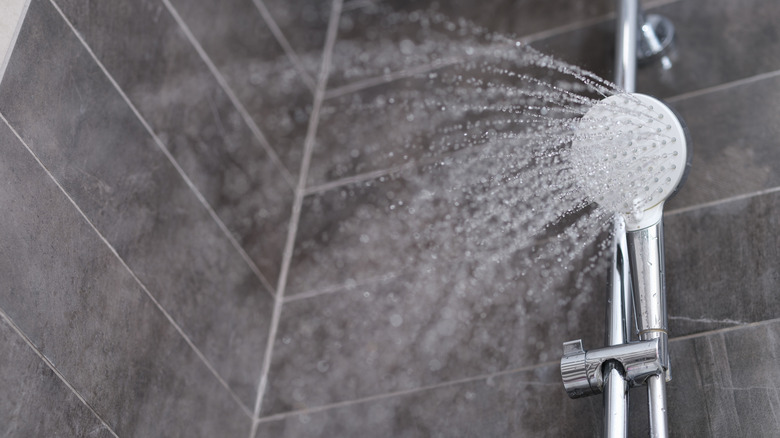 A shower head spraying water, dark tiles in the background