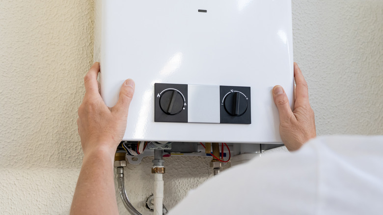 Person installing a tankless hot water heater on a wall.