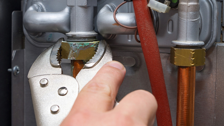 Close up of a man using vice grips to loosen a partially corroded nut from a plumbing system.