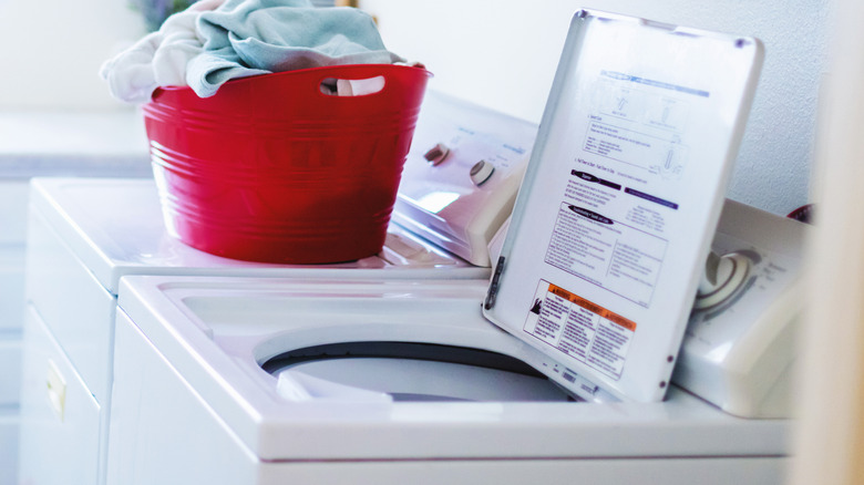 A top-load washing machine opened next to a full laundry basket.