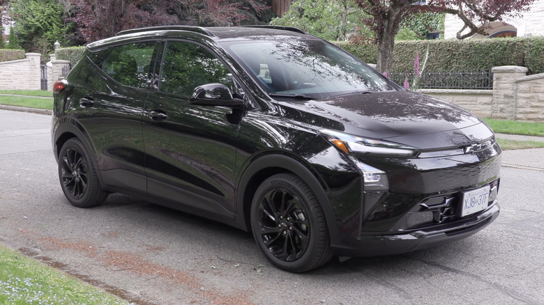 A black 2026 Chevrolet Bolt EV with black wheels in a suburban neighborhood, front 3/4 view