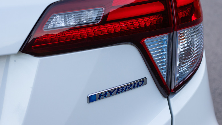 A white car with a hybrid badge underneath the tail lights