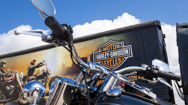 Close-up of cruiser motorcycle handlebars with Harley-Davison truck in background.