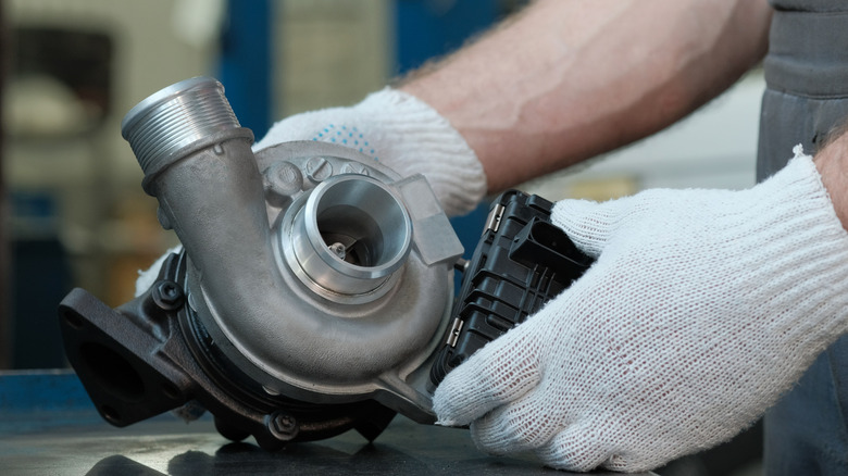 Close-up of gloved hands holding turbocharger on metal surface.