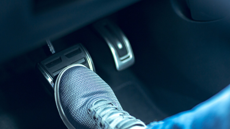 Close-up of foot near accelerator and brake pedals.