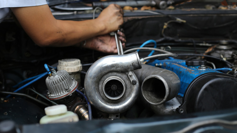Man performing work on car engine with turbocharger installed.