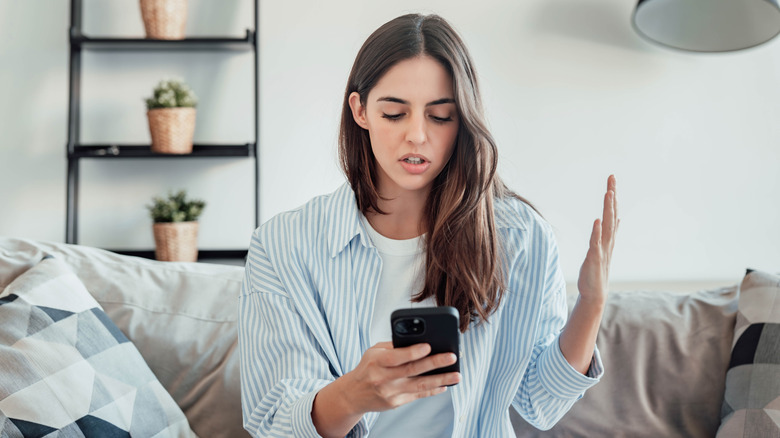 Woman looking at phone with frustrated expression and gesture.