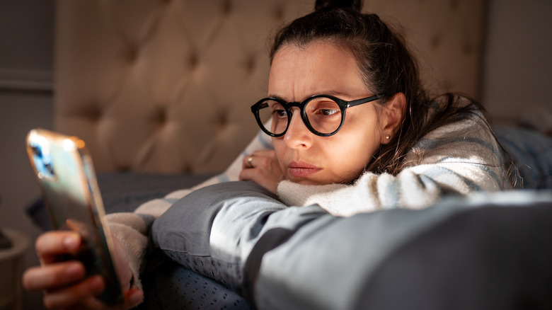 Woman looking at phone with unimpressed expression.