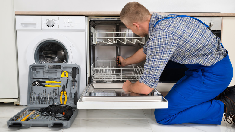 person repairing a dishwasher with a tool box placed on the floor